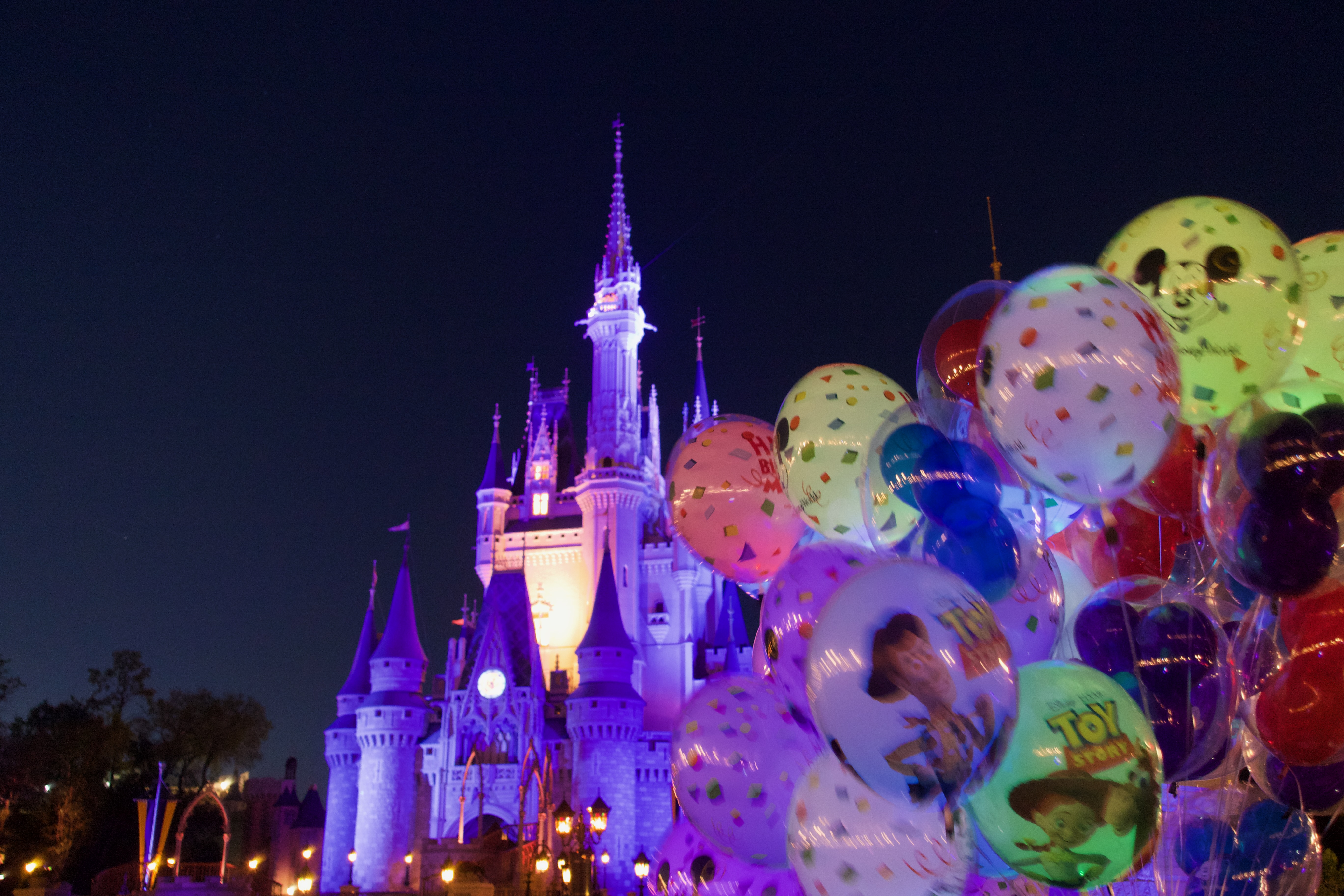 Magic Kingdom Cinderella Castle at night with colorful Disney balloons in the foreground