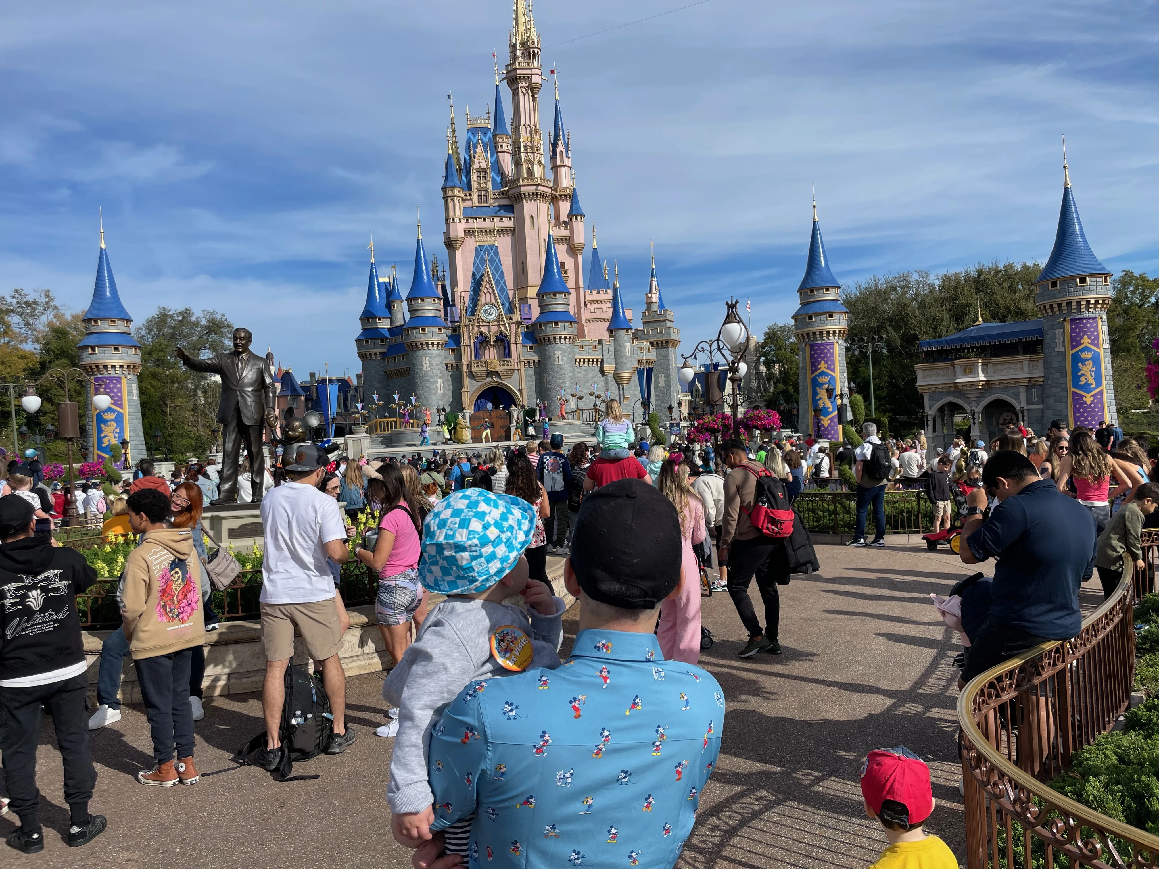 Families walking toward Cinderella Castle with luggage and Disney gear